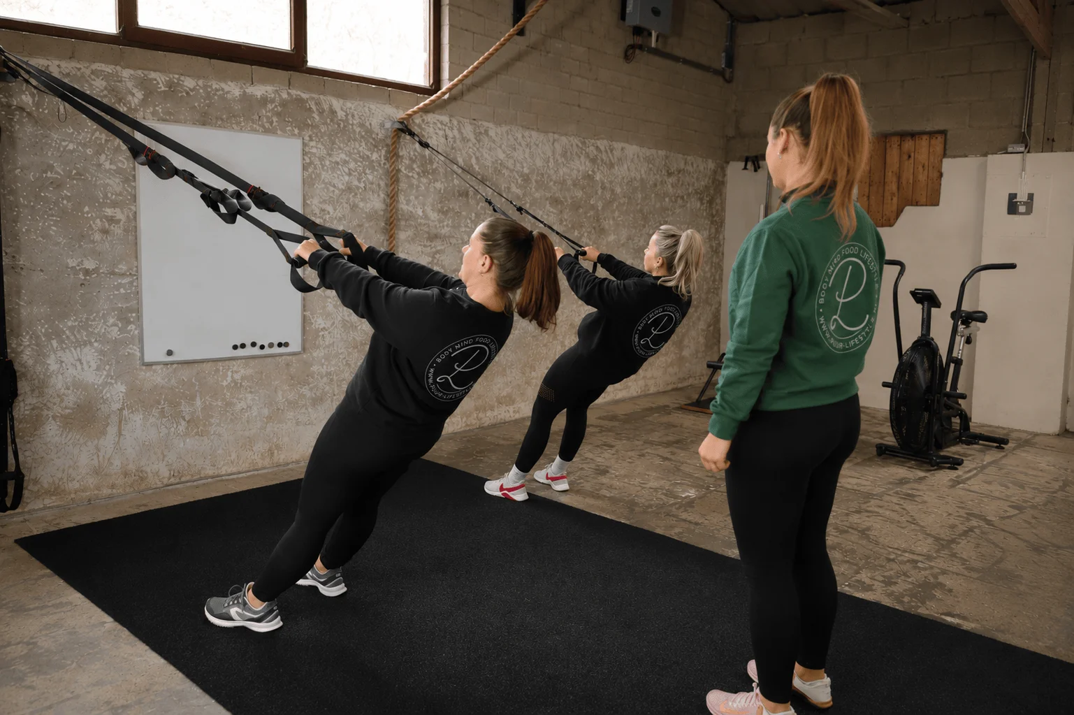 Trudy coacht twee vrouwen die TRX-rows uitvoeren